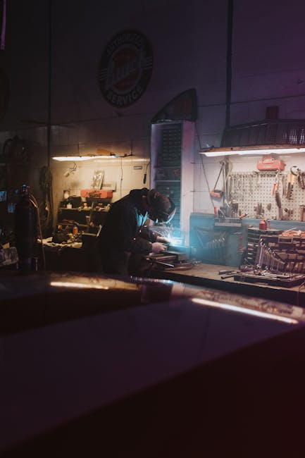 A mechanic focuses on repairing equipment in an industrial garage setting illuminated by neon lights.